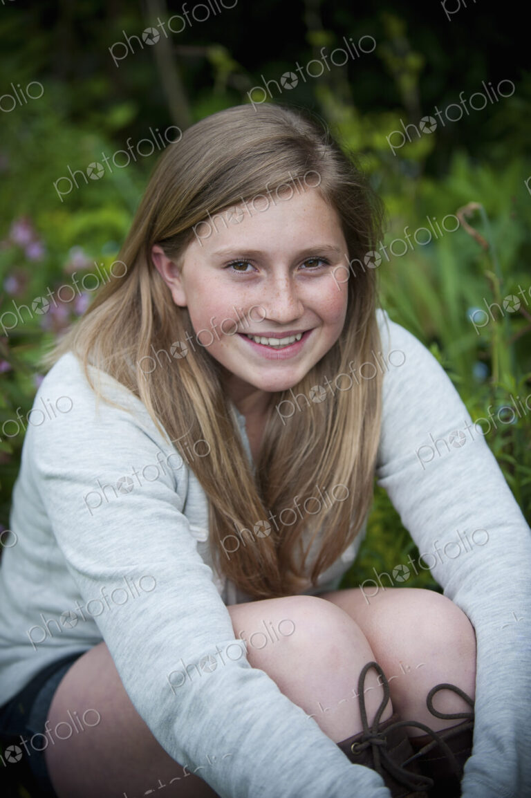 A teenage girl with brunette hair sitting in a garden.