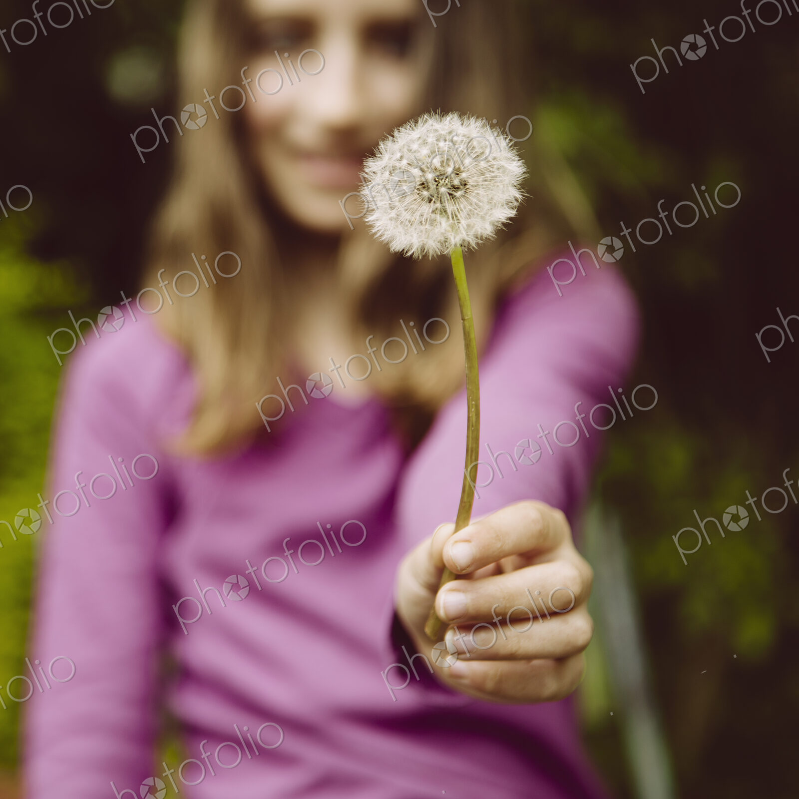 A ten year old girl holding a dandelion clock seedhead on a long stem.