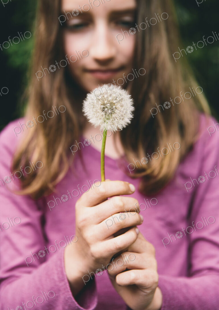 A ten year old girl holding a dandelion clock seedhead on a long stem.