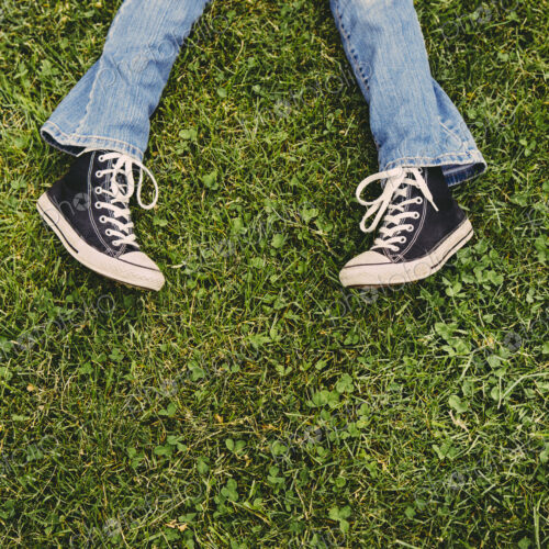 A ten year old girl lying on the grass. Cropped view of her lower legs. Wearing…