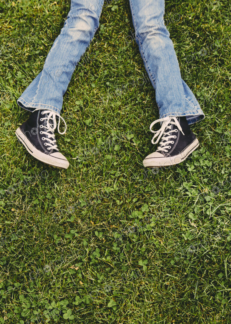 A ten year old girl lying on the grass. Cropped view of her lower legs. Wearing…