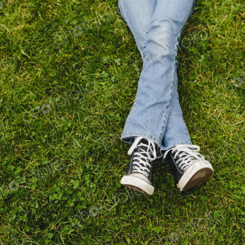 A ten year old girl lying on the grass. Cropped view of her lower legs. Wearing…