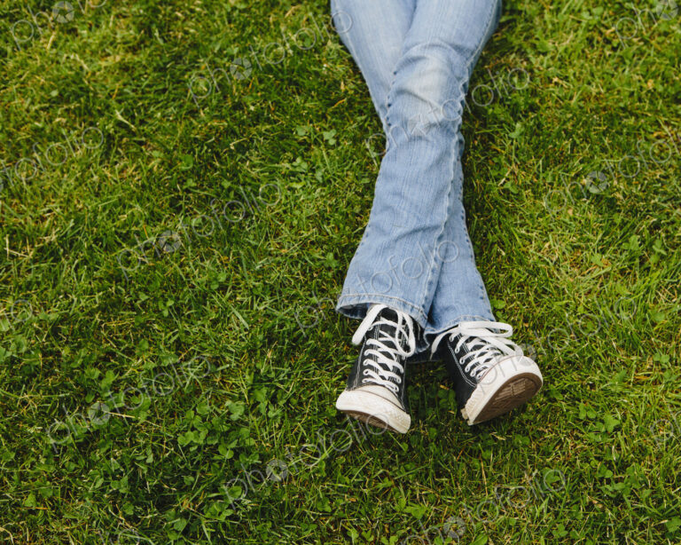 A ten year old girl lying on the grass. Cropped view of her lower legs. Wearing…