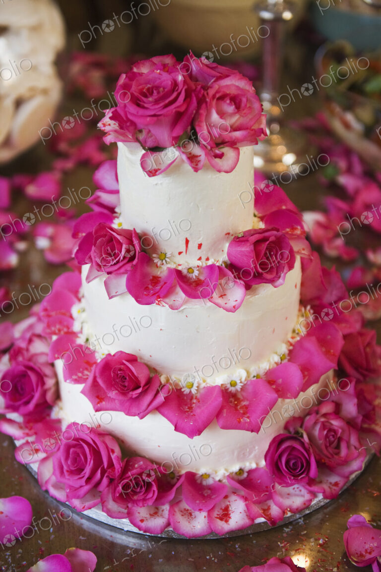 A three tiered wedding cake, covered in white frosting and decorated with pink rose…