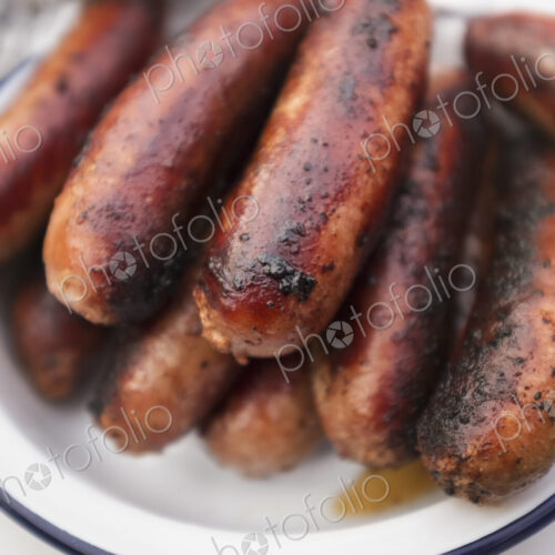 A tin plate stacked with cooked sausages on a table. A tin plate stacked with cooked sausages on a table.