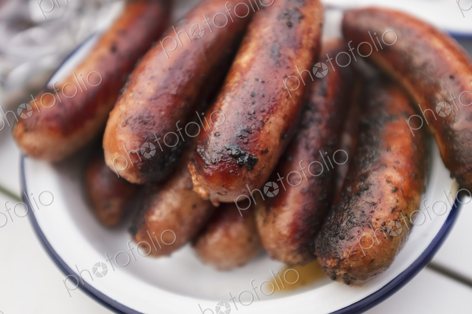 A tin plate stacked with cooked sausages on a table.