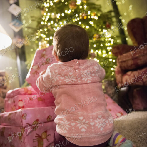 A toddler beside a pile of presents under a Christmas tree. A toddler beside a pile of presents under a Christmas tree.