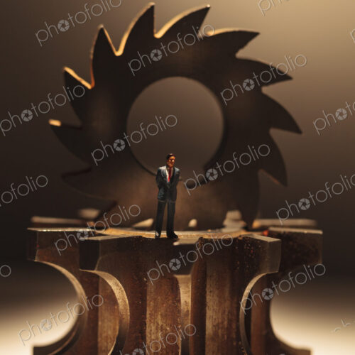 A toy model of a Businessman standing by three stacked cog wheels with different gearing.