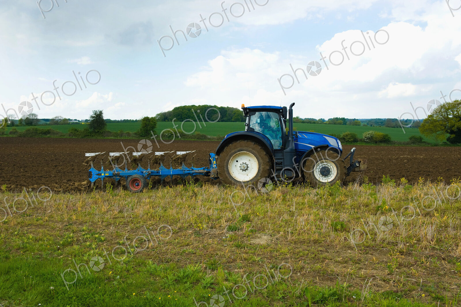 A tractor harrowing, ploughing in the stubble in a field.