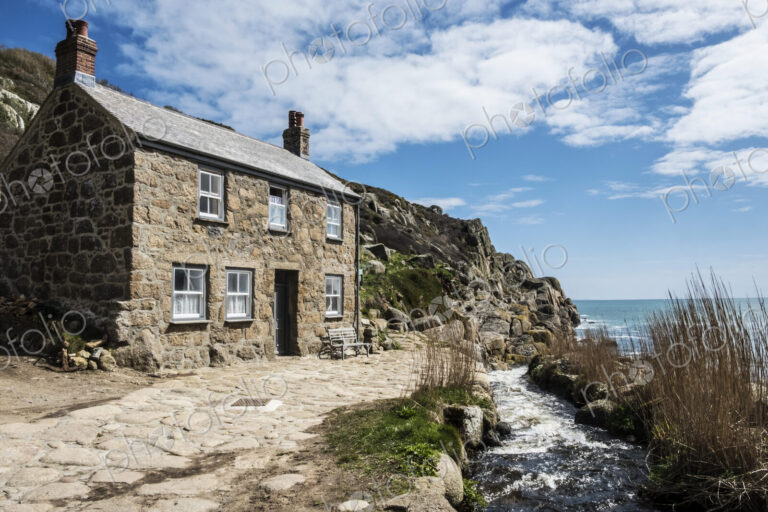 A traditional stone built cottage on the coast, with a path past the front door.