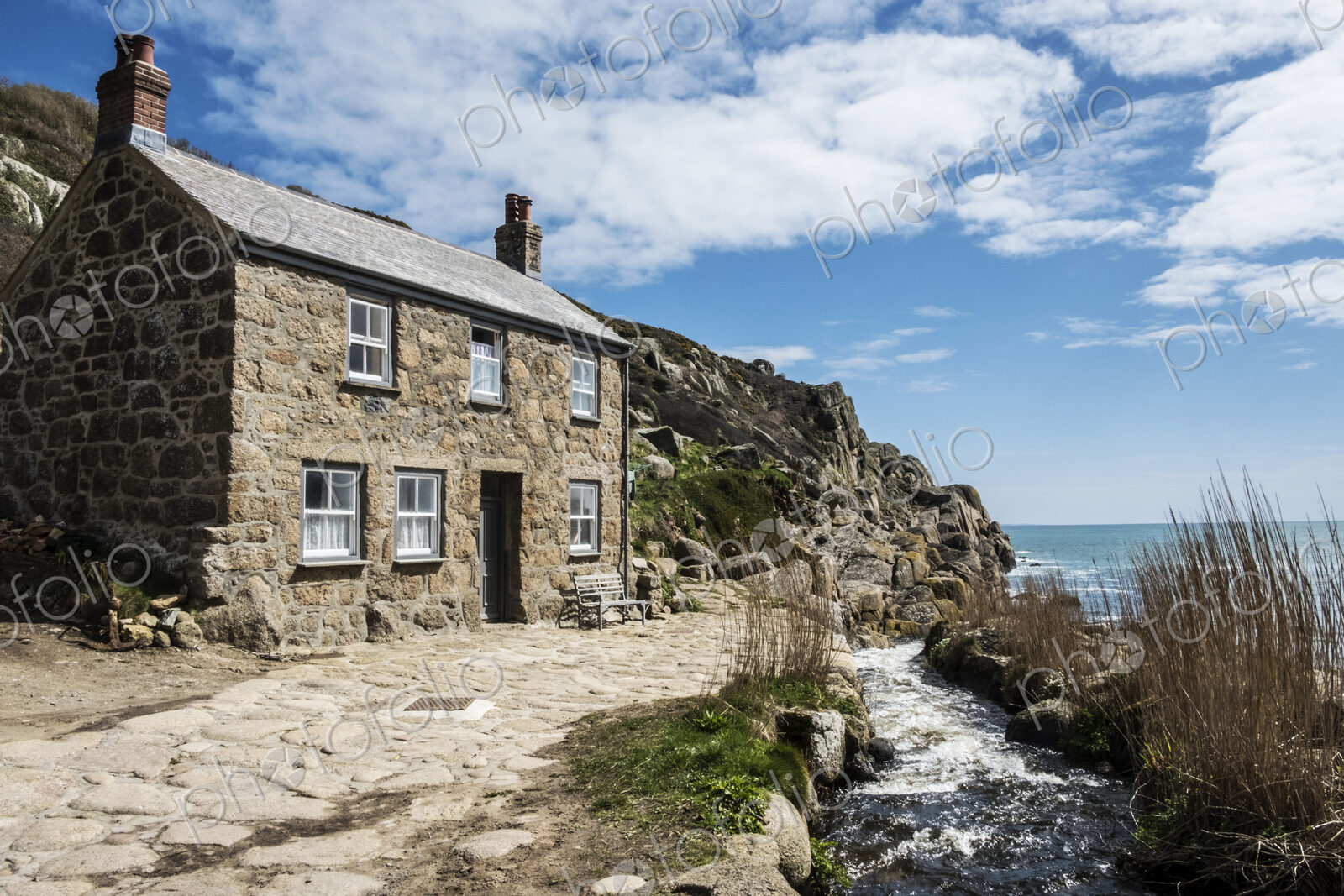 A traditional stone built cottage on the coast, with a path past the front door.