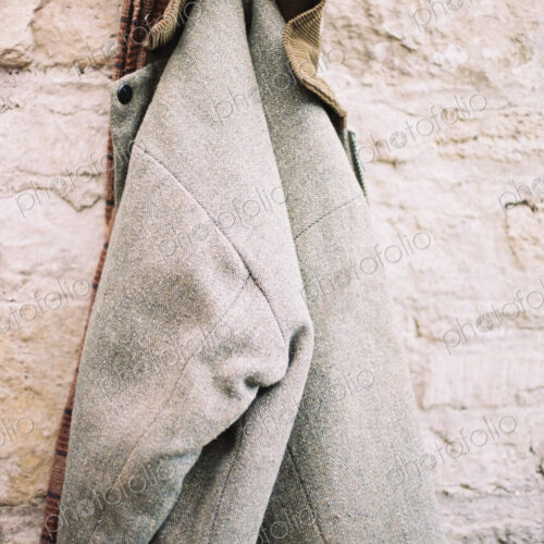 A traditional warm jacket with corduroy collar hanging from a pen on a stone wall.
