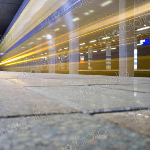 A train passing through a station, surface view, a trail of lights and motion blur.