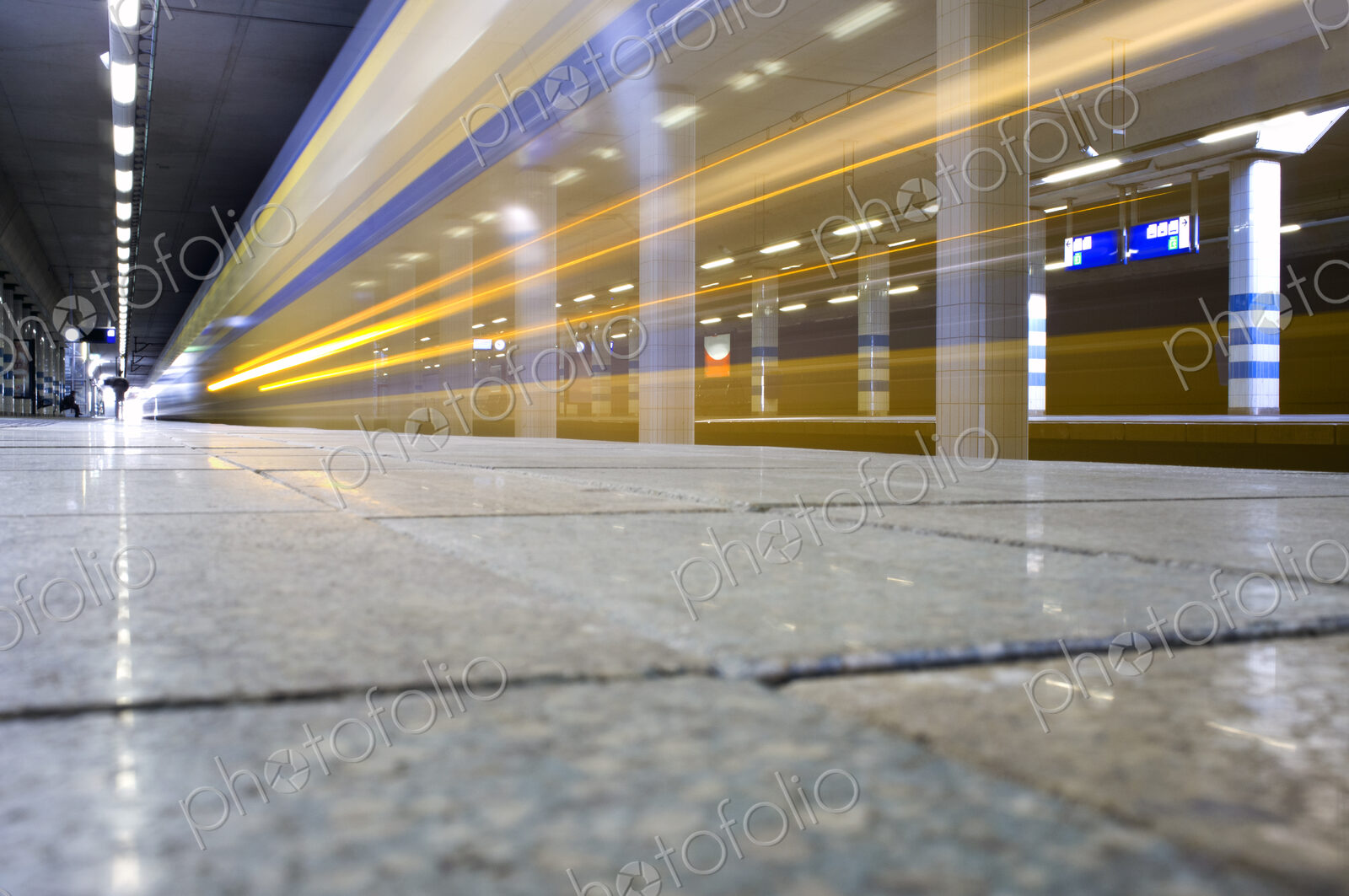 A train passing through a station, surface view, a trail of lights and motion blur.