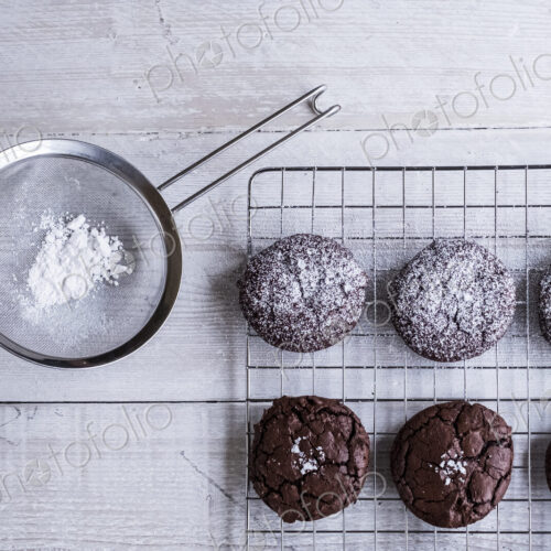 A tray of cooling chocolate brownies, and a sieve with icing sugar for decoration.