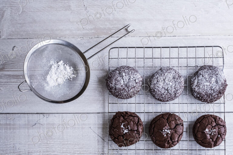 A tray of cooling chocolate brownies, and a sieve with icing sugar for decoration.