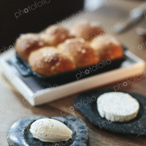 A tray of freshly baked bread rolls and cheese on a table top at a city restaurant.