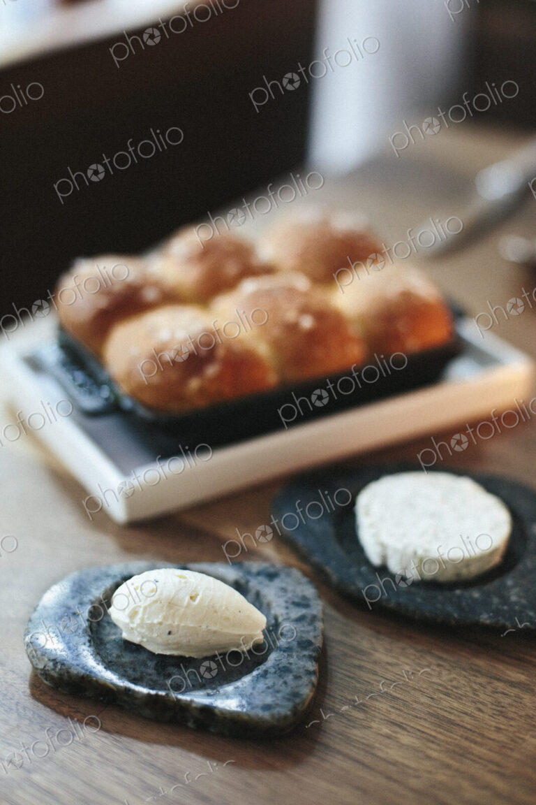 A tray of freshly baked bread rolls and cheese on a table top at a city restaurant.