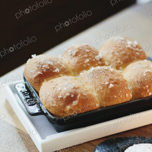 A tray of freshly baked bread rolls and cheese on a table top at a city restaurant.