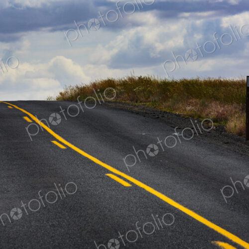 A two lane road with yellow central line, one solid and one broken through countryside. A two lane road with yellow central line, one solid and one broken through countryside.
