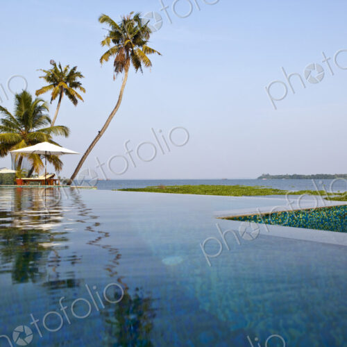 A view across flat calm waters, the backwaters of the state of Kerala, low lying land…
