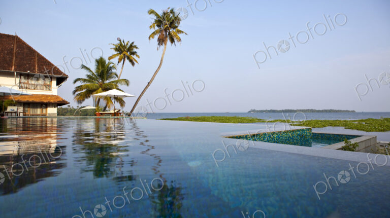 A view across flat calm waters, the backwaters of the state of Kerala, low lying land…