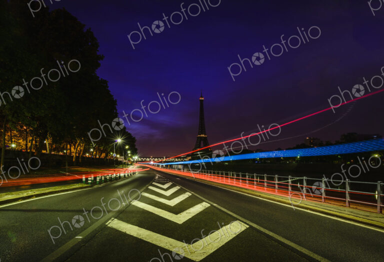 A view along a city road at night, tall buildings and light trails, the Eiffel tower…