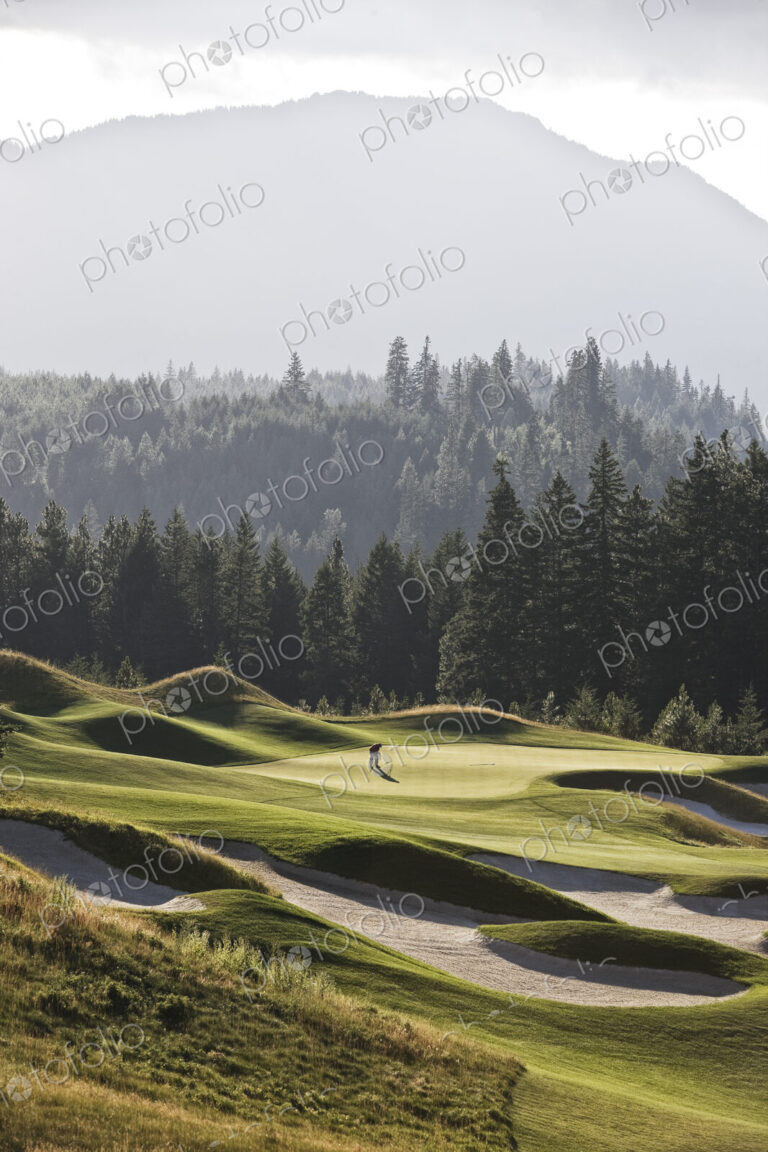 A view from a distance of a single golfer on a greeen of a golf course.