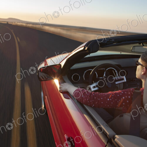 A view from above looking down on a Caucasian woman driving a convertible sports car. A view from above looking down on a Caucasian woman driving a convertible sports car.