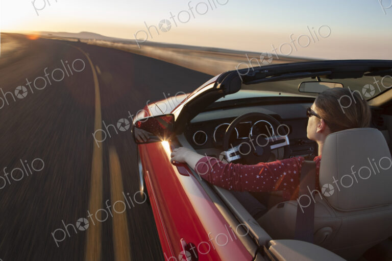 A view from above looking down on a Caucasian woman driving a convertible sports car.