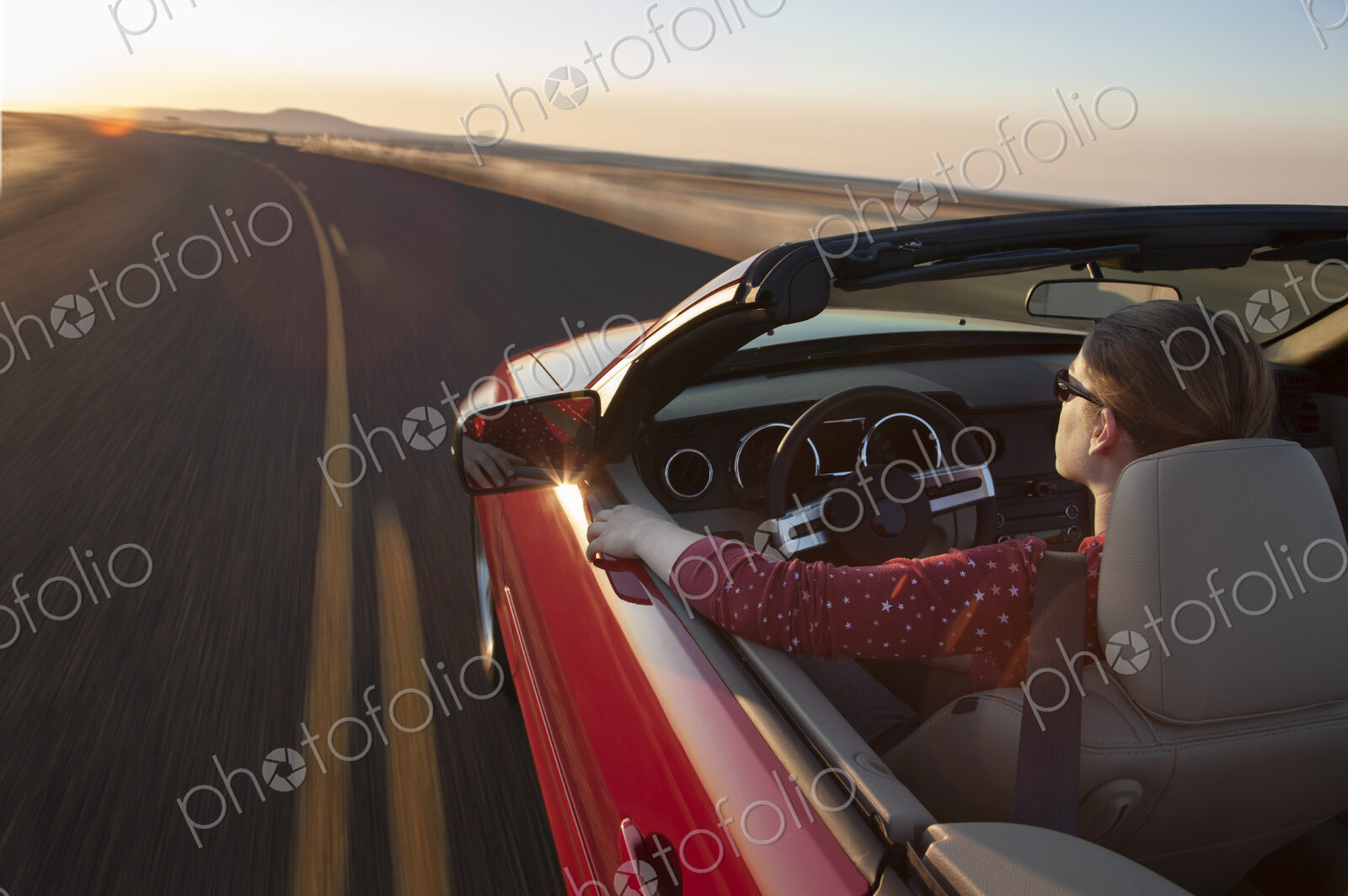 A view from above looking down on a Caucasian woman driving a convertible sports car.