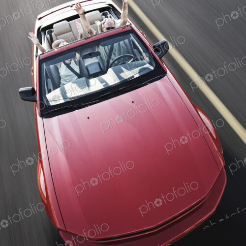 A view from above looking down on a convertible sports car and a Caucasian couple on a…