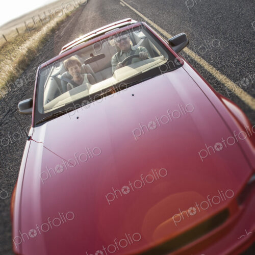 A view from above looking down on a convertible sports car and a Caucasian couple on a…