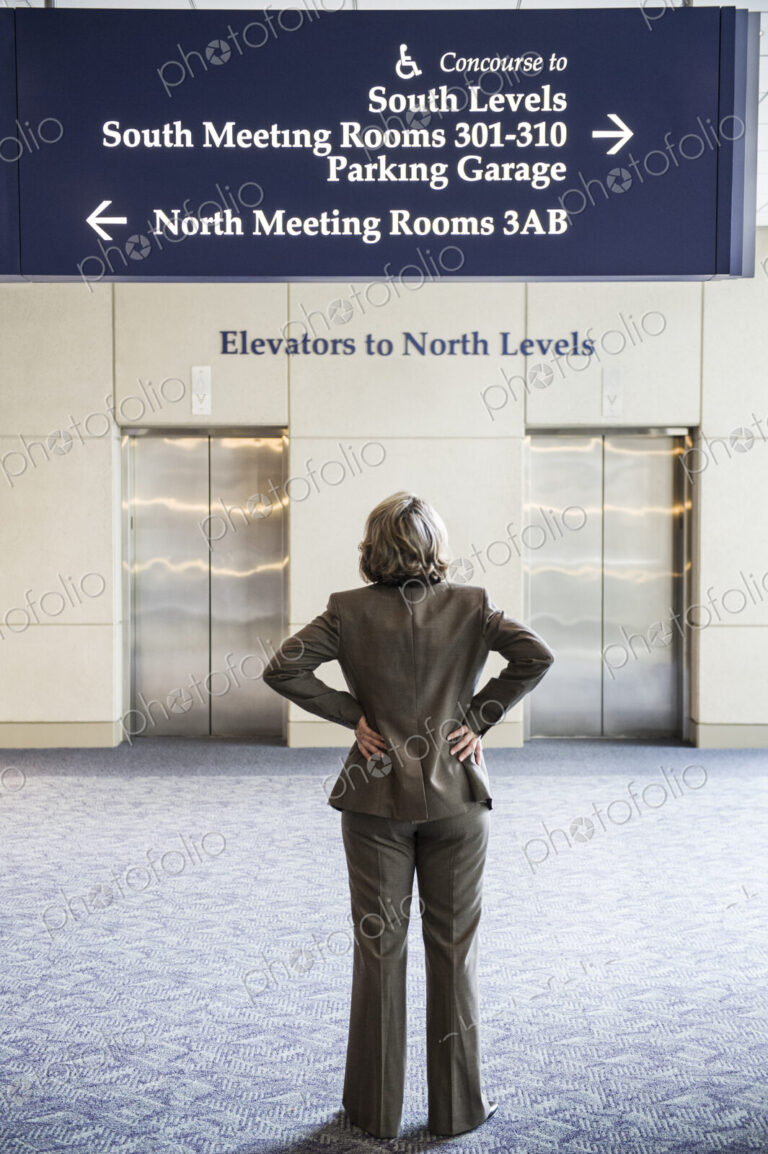 A view from behind of a businesswoman looking at sinage directions in a convention center.
