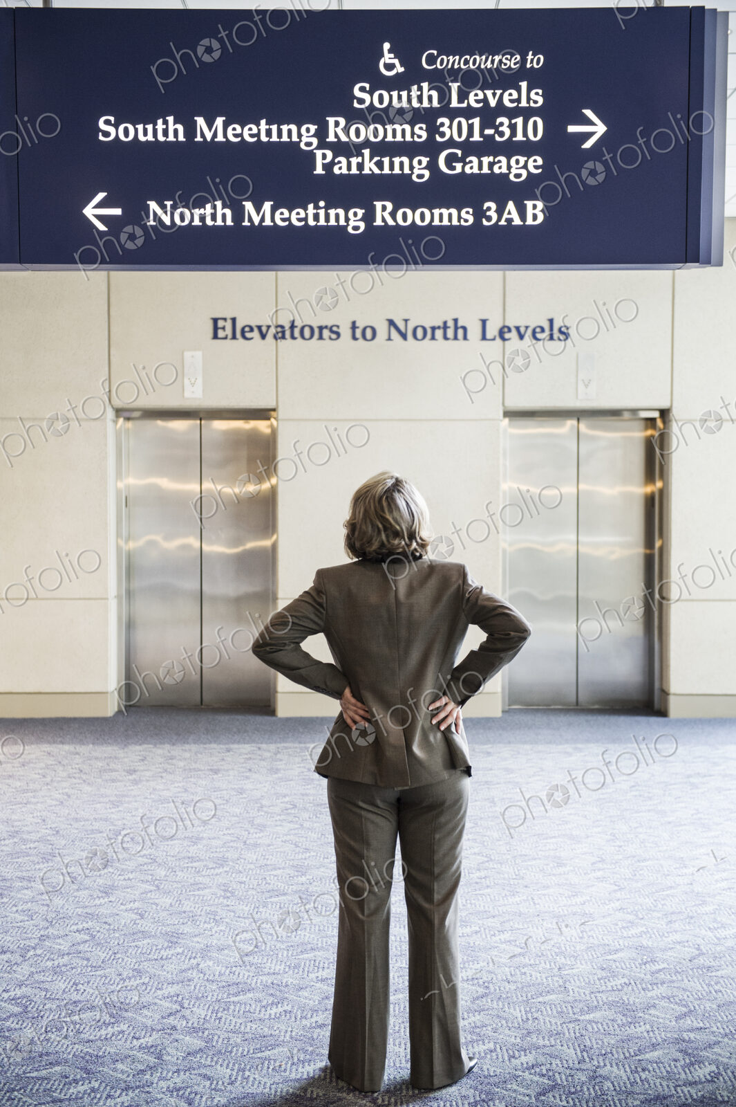 A view from behind of a businesswoman looking at sinage directions in a convention center.