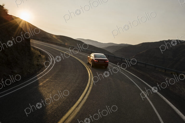A view from behind of an automobile going around a curve at sunset in eastern…