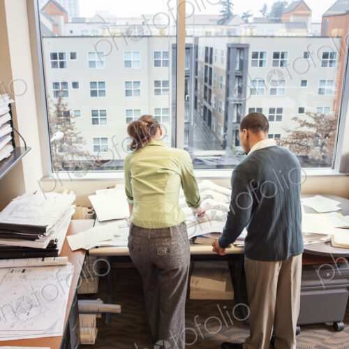 A view from behind of two people going over plans for a new space in their office. A view from behind of two people going over plans for a new space in their office.