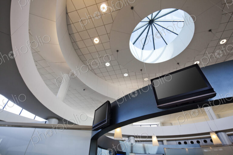 A view from below to a round dome ceiling with a central skylight. Display screens.