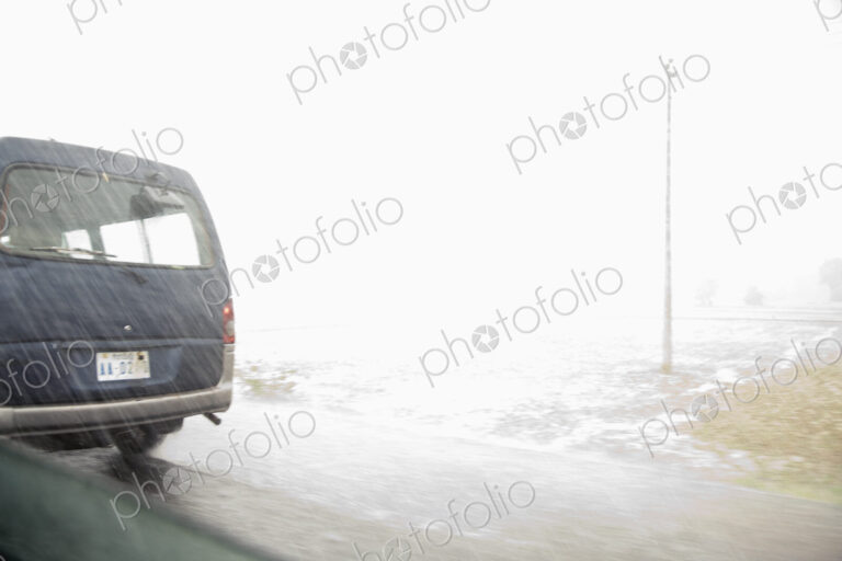 A view from inside a car of the monsoon rain falling on a road.