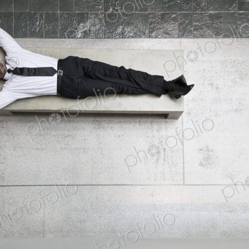 A view looking down on a businessman taking a break laying down on a bench. A view looking down on a businessman taking a break laying down on a bench.
