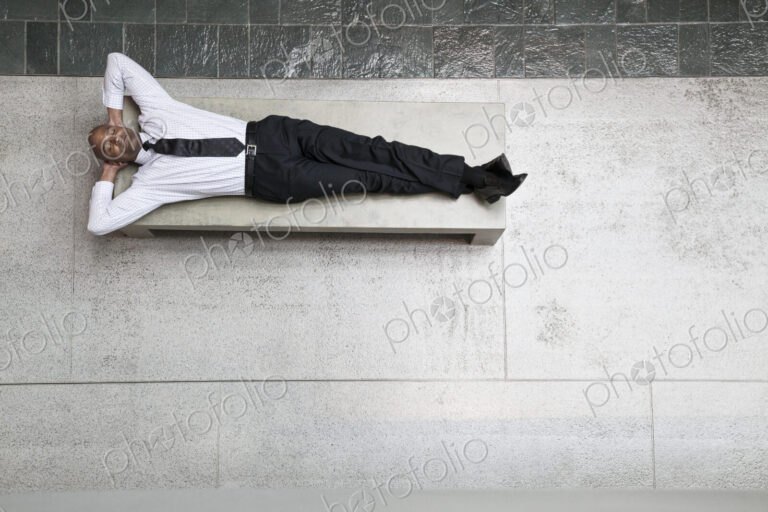 A view looking down on a businessman taking a break laying down on a bench.