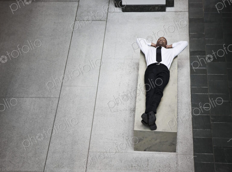 A view looking down on a businessman taking a break laying down on a bench.