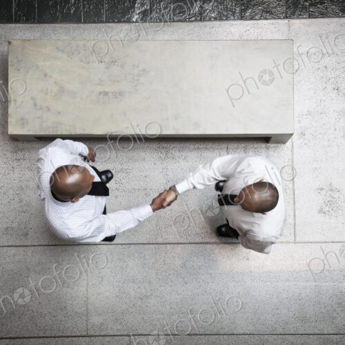 A view looking down on two businessmen shaking hands in an office lobby. A view looking down on two businessmen shaking hands in an office lobby.