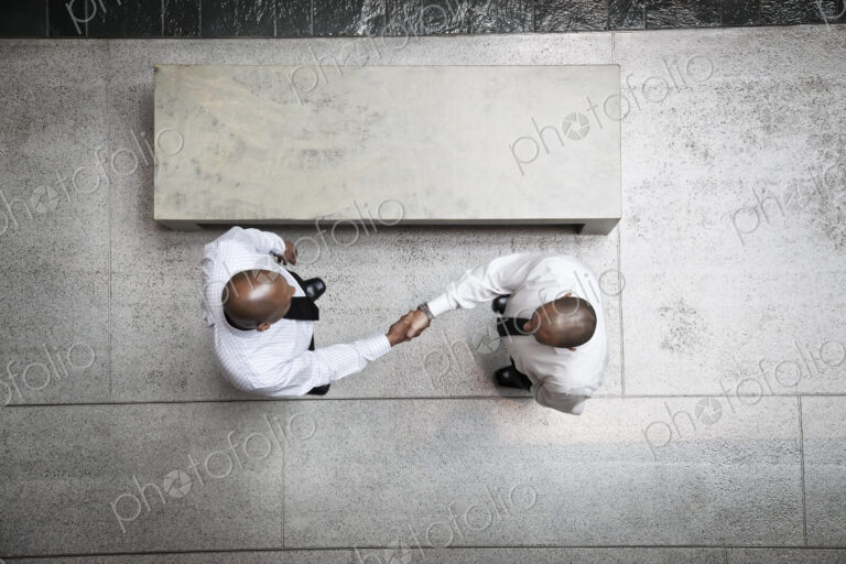 A view looking down on two businessmen shaking hands in an office lobby.