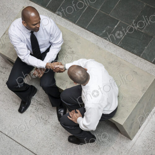 A view looking down on two businessmen shaking hands in an office lobby. A view looking down on two businessmen shaking hands in an office lobby.