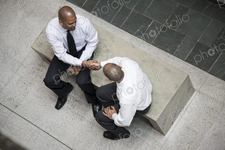 A view looking down on two businessmen shaking hands in an office lobby.