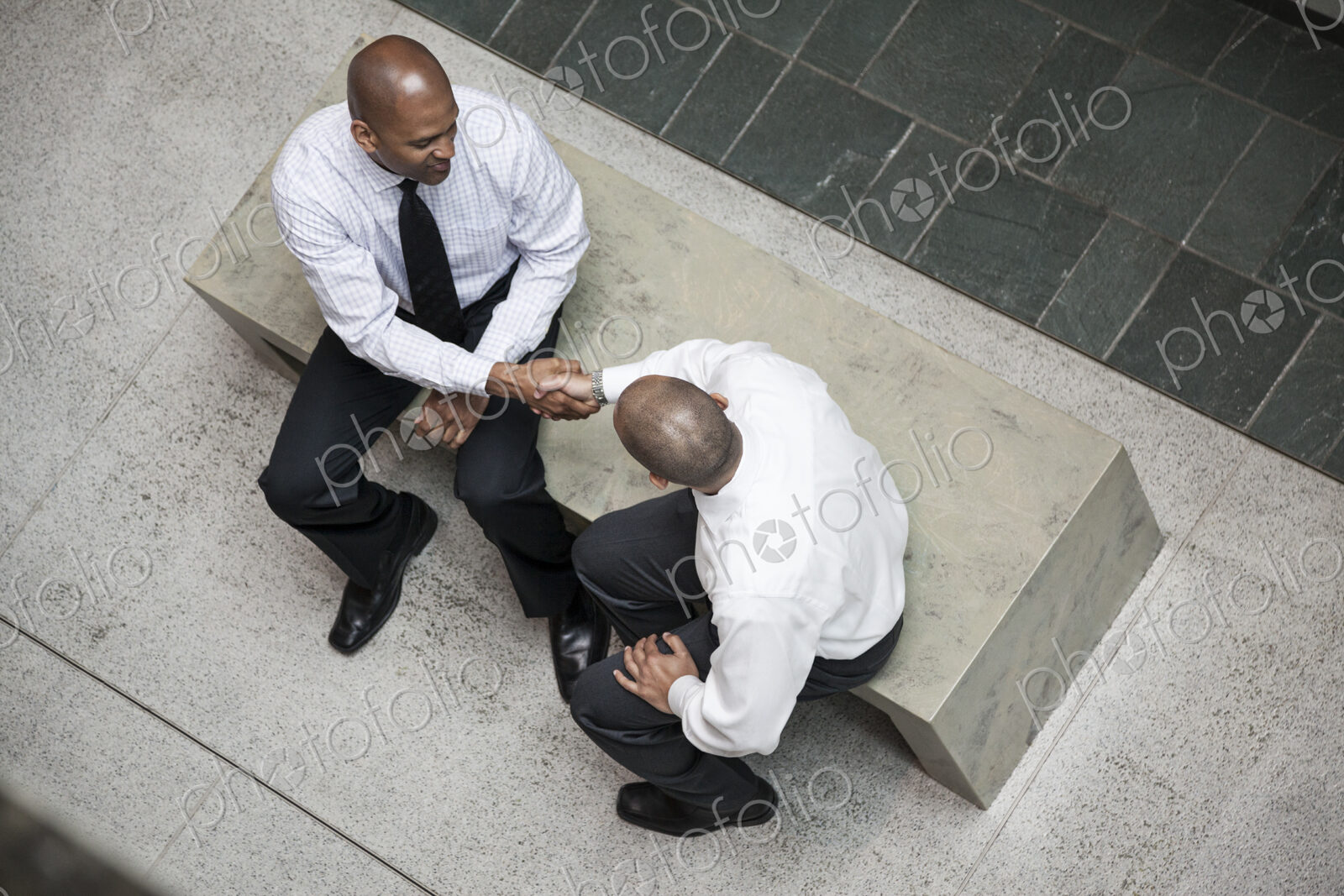 A view looking down on two businessmen shaking hands in an office lobby.
