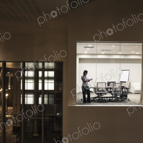 A view looking into a conference room at night of an Asian businesswoman.