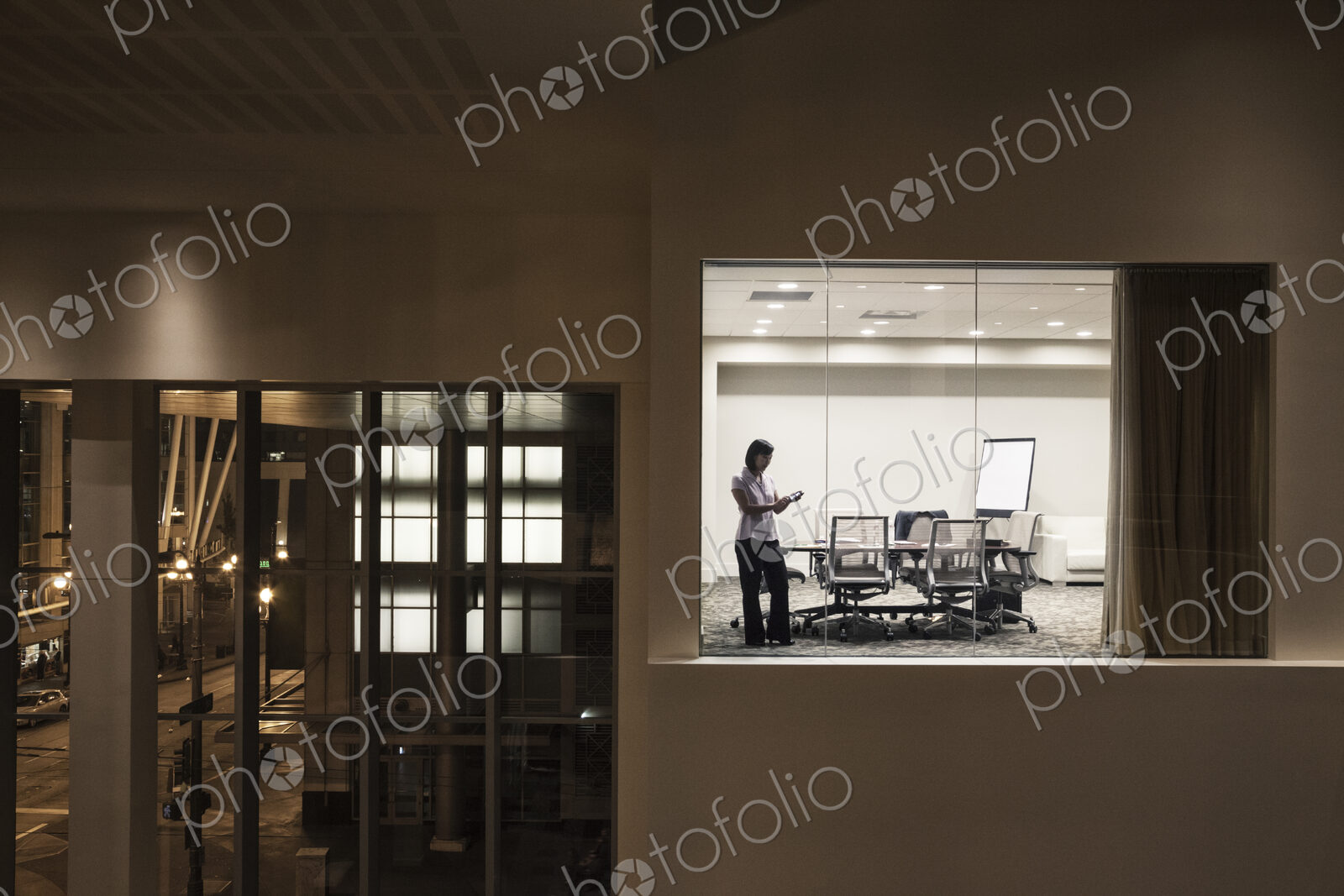 A view looking into a conference room at night of an Asian businesswoman.