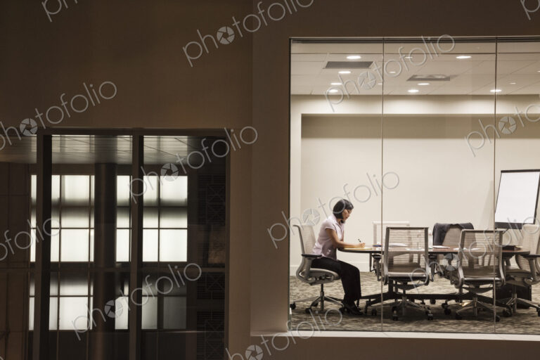 A view looking into a conference room at night of an Asian businesswoman.
